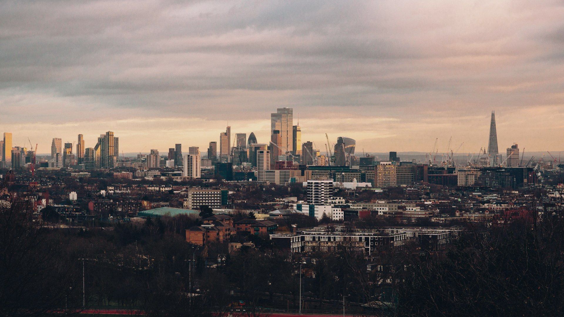 London skyline of period rooftops and distant towers under a bright overcast sky.