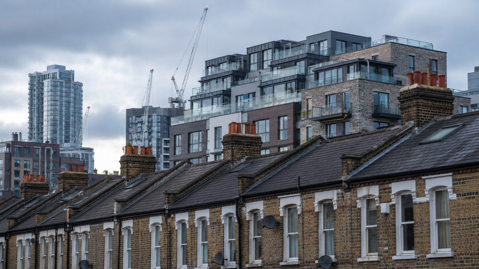 New build balconies rising behind a row of Victorian terraces, cranes faint in the distance.