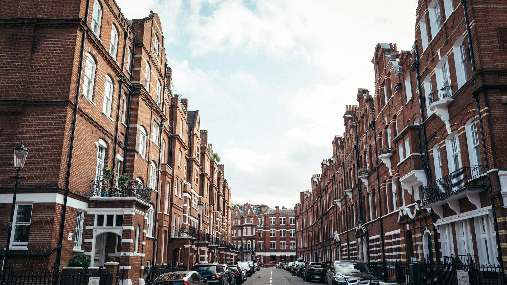 A quiet London street of red brick mansion blocks with black railings and street lamps