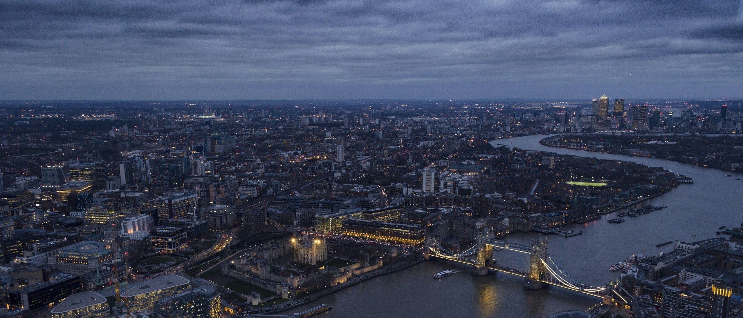 London at blue hour from above, the Thames winding past Tower Bridge through the lit city