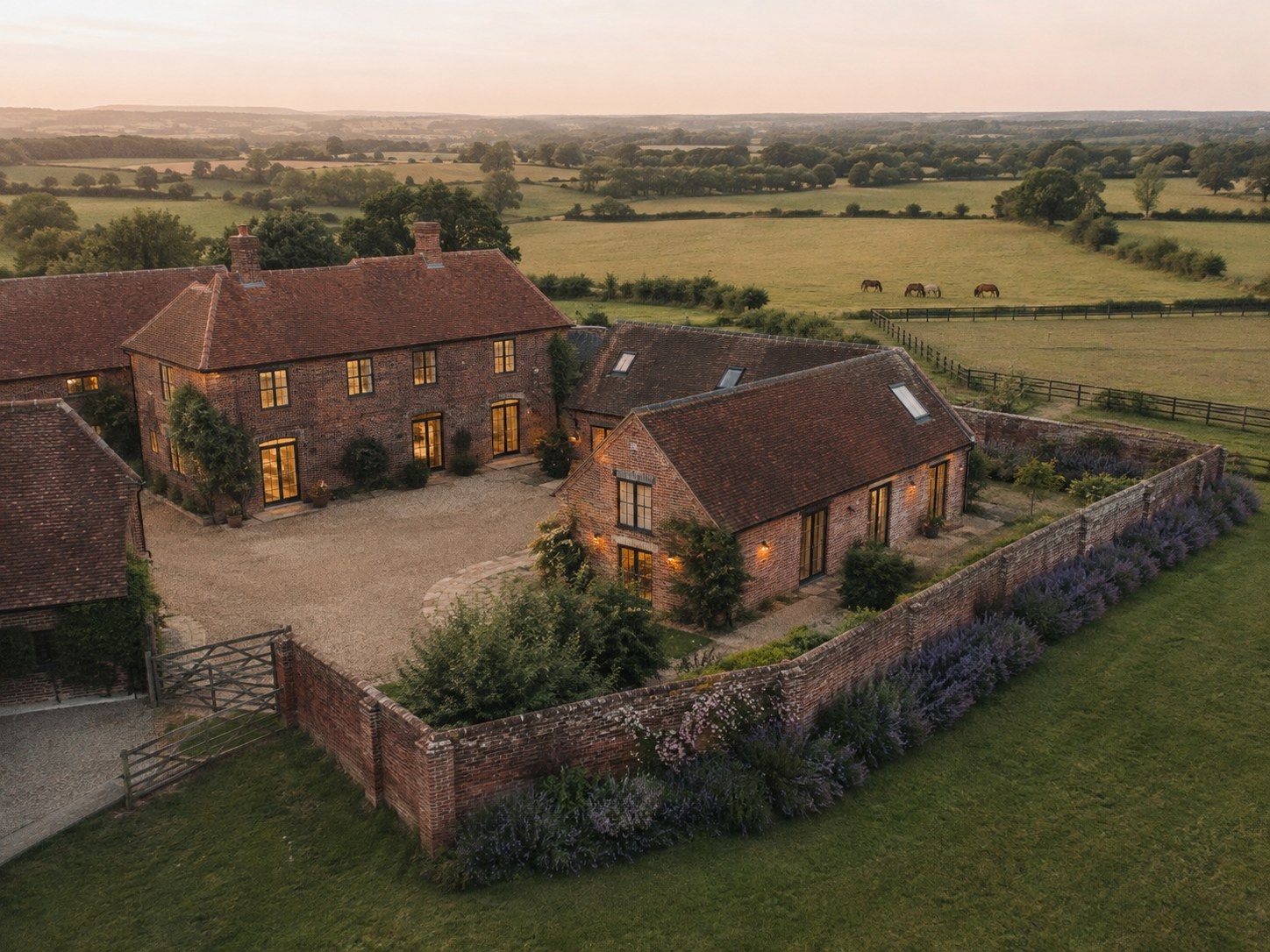 Red brick country house with barn wings at dusk, a walled garden edged with lavender and paddocks beyond