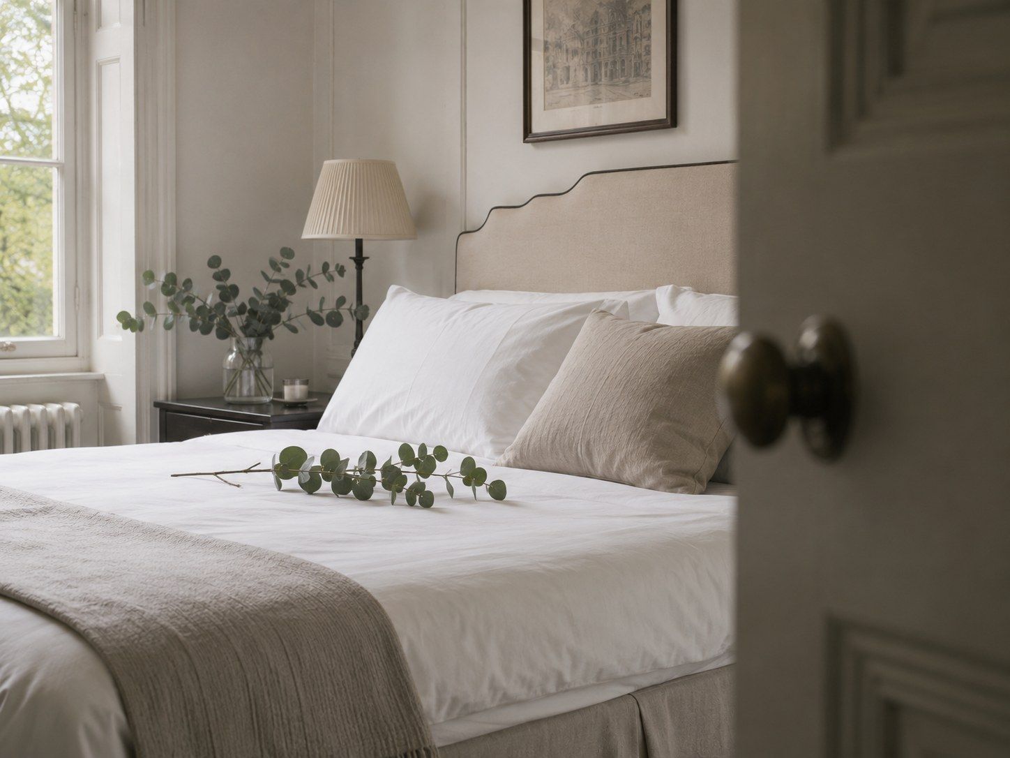 Pressed white linens and fresh eucalyptus on a bed in a bright bedroom